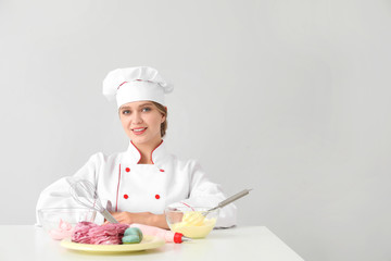 Female confectioner with tasty desserts on light background