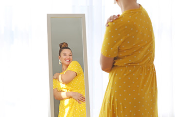 Young body positive woman looking in mirror at home