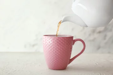  Gieten van hete thee uit theepot in beker op tafel © Pixel-Shot