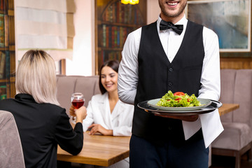 Young male waiter with salad in restaurant