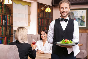 Young male waiter with salad in restaurant