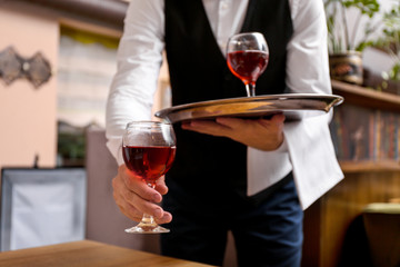 Young male waiter with glasses of wine in restaurant, closeup