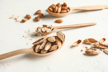 Spoons with tasty almonds on white background