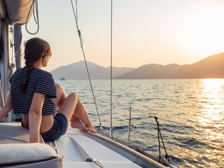 attractive young woman in a striped t-shirt enjoys the sunset on the deck of a sailing yacht....