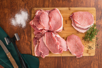 Raw Boneless Pork Loin chops on wooden cutting board with some herbs, salt, and rosemary close up...