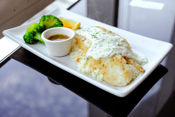 Grilled Pangasius with rice and white cream sauce on the plate.