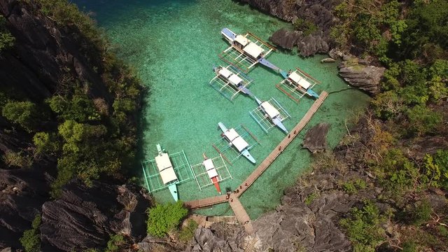 Flying tourist camera drone over a naturally shallow water sheltered harbor sandy cove caused by wind and water erosion, which now serves as a wooden boardwalk docking area or tour boats