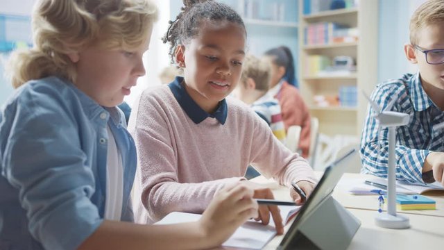 In the Elementary School: Class of Smart Young Children Work as a Team Using Tablet Computers to Program Wind Turbines. Classroom with Kids Learning about Eco-Friendly Forms of Renewable Energy