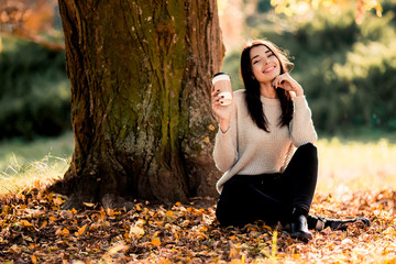 Beautiful woman drink coffee sitting in autumn park.