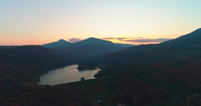 Levee drone aerial at sunrise with hills and mountains in Hungary, Hasznos. Sun rises behind the hills, reflections on the water.