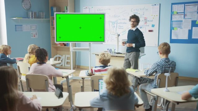 In the Elementary School Classroom: Teacher Uses Horizontal Green Mock-up Screen Interactive Digital Whiteboard to Explain Lesson to Diverse Group of Schoolchildren. Multi Ethnic Kids Learning Science