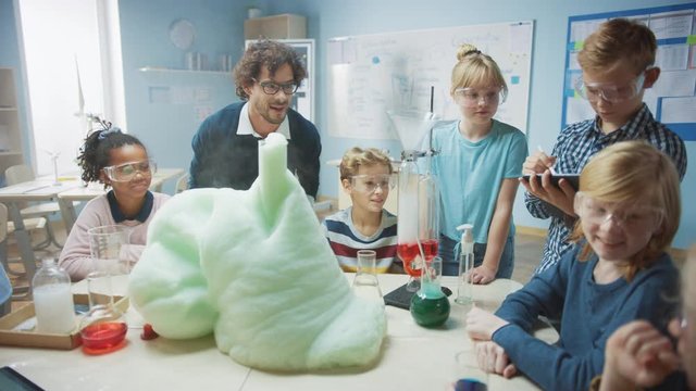 Elementary School Science / Chemistry Classroom: Enthusiastic Teacher Shows Funny Chemical Reaction Experiment to Group of Children. Mixing Chemicals in Beaker so they Shoot Foam (Elephant Toothpaste)