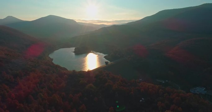Levee drone aerial at sunrise with hills and mountains in Hungary, Hasznos. Sun rises behind the hills, reflections on the water.