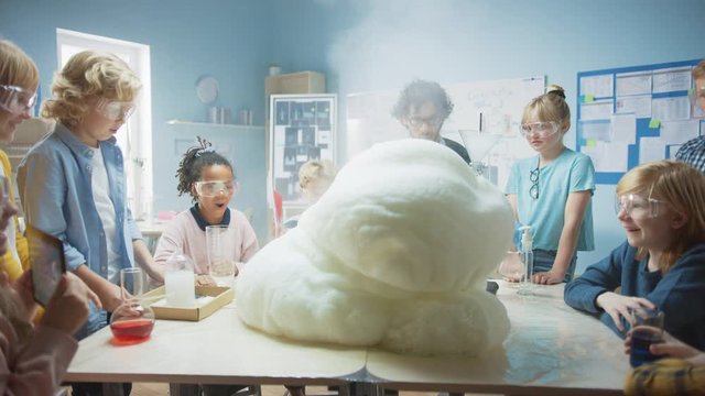Elementary School Science / Chemistry Classroom: Enthusiastic Teacher Shows Funny Chemical Reaction Experiment to Group of Children. Mixing Chemicals in Beaker so they Shoot Foam (Elephant Toothpaste)