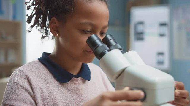 Portrait of Smart Little Schoolgirl Looking Under the Microscope. In Elementary School Classroom Cute Girl Uses Microscope. STEM (science, technology, engineering and mathematics) Education Program