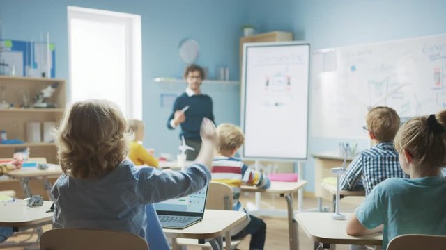 Elementary School Physics Teacher Uses Interactive Digital Whiteboard to Show to a Classroom full of Smart Diverse Children how Generator Works. Science Class, Kid Raises Hand with Answer