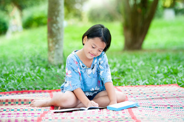 Beautiful asian little girl draws a picture in the park using a color pencil with paints and drawing note book. Learning and drawing in green park,Portrait of happy little girls child with smiling.