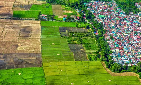 Aerial view showing expansion of urbanization and mass housing into agricultural land and rice fields in southeast Asia. Luzon island, Philippines.