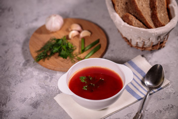 Beetroot soup with parsley in a plate. Tasty and hearty dinner. Borsch with vegetables on a gray background.