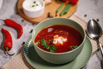 Beetroot soup with sour cream and herbs in a plate, close-up. Tasty and hearty dinner. Borsch with vegetables on a gray background.
