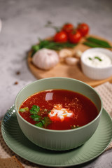 Beetroot soup with sour cream and herbs in a plate, close-up. Tasty and hearty dinner, borsch with vegetables. Still life
