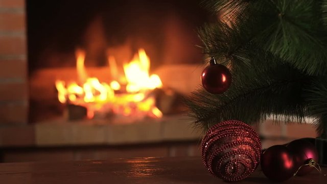 small Christmas tree with decorations stands on the table against the background of a burning fireplace. Red Christmas balls. Celebration and fun by the fireplace.