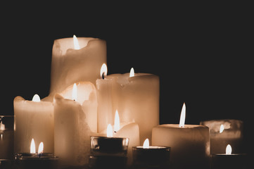 Composition of burning candles close-up on a dark background. Melted wax candles of different...