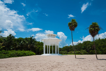 White gazebo on a beach with palm trees, blue sky background, Mexico
