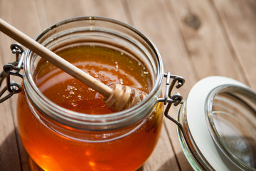 Honey in glass jar on a wooden floor.