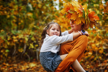Portrait of a little girl and mother in the autumn Park, a girl with a wreath of maple leaves .