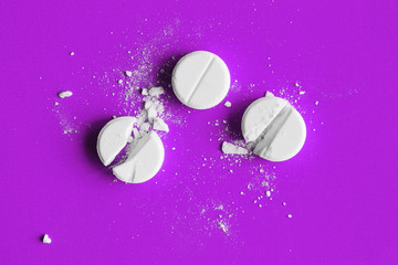 Obraz na płótnie Canvas Three white crushed pills on purple background. Broken tablets. Closeup. Flat lay