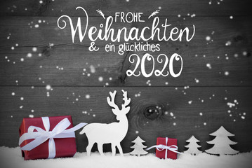 German Calligraphy Frohe Weihnachten Und Ein Glueckliches 2020 Means Merry Christmas And A Happy 2020. Red Christmas Decoration Like Tree, Gift, And Reindeer. Black Wooden Background With Snowfalkes