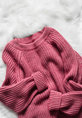 Color raspberry woolen women's sweater on a white fluffy carpet, top view. Fashion concept