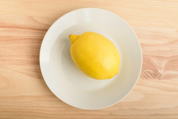 One yellow lemon on a white plate on a wooden brown table, top view or flat lay photo of  healthy food