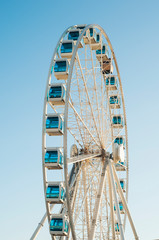 White ferris wheel with blue booths on the background of a blue sky. Amusement park.