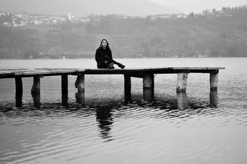 The young girl sitting on the dock on the lake