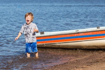 little cute redhead Caucasian boy enjoying splashes of water near boat in the lake playing funny game with parents in summer sunny day - Powered by Adobe