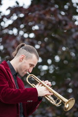 Obraz premium young handsome trumpeter playing jazz on his gold trumpet in autumnal park 