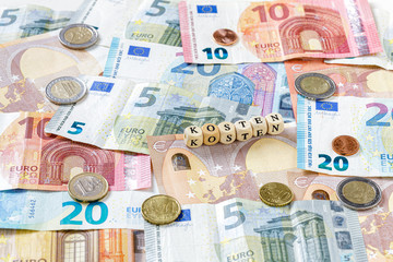 Kosten Schriftzug über Euro Geldscheinen und Münzen, Nahaufnahme
