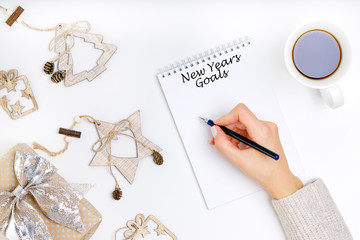 Young woman is writing goals on notebook, new year resolutions concept. Top view, flat lay.