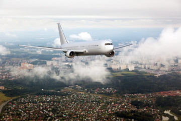 Passenger plane in flight. Aircraft flyes through the clouds above the buildings of city quarters.