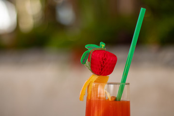 Orange fruit cocktail with green plants and red flowers background