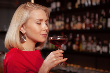 Close up of a beautiful blond woman smiling with her eyes closed having a drink at the bar in the evening