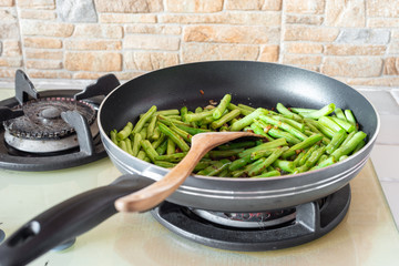 Home cooked food. French green beans, dried chillies and garlic in stir-fry pan on cooking stove