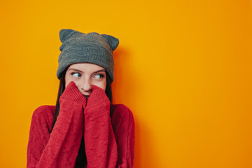 Woman in gray hat on the orange background. Young woman in sweater and hat. Winter is coming. Woman is hiding in sweater.