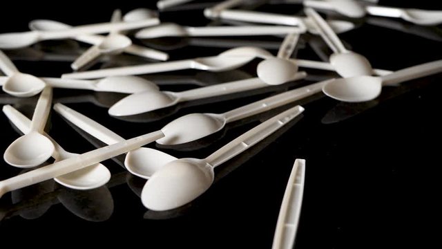 Variety of white plastic spoons are thrown from above on a specular black table