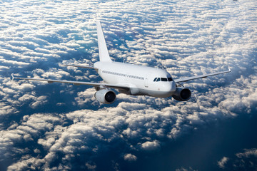 Naklejka na ściany i meble White passenger plane flies high over the clouds.