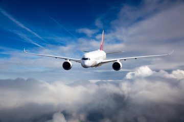 White passenger plane in flight. The plane flies against a background of a cloudy sky. Aircraft front view.