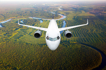 White passenger plane in flight. The plane flies against a background of a forest and river....