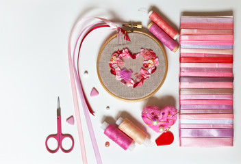 Process of embroidering pink heart with ribbons for Valentine's Day and accessories: needles, pins, threads, scissors and set of ribbons (embroidery was made by author of photo). Copy space, flat lay
